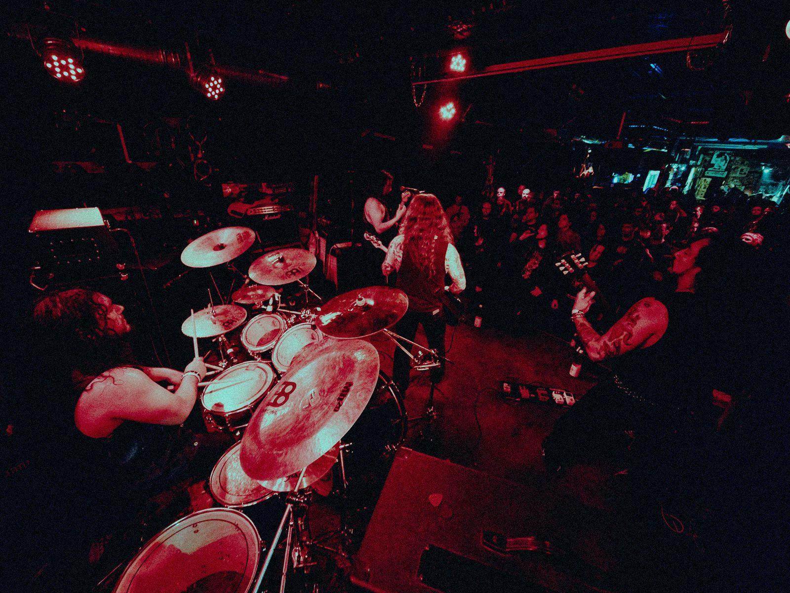 Haunter performing on a small stage, shot from behind the drummer looking out towards the crowd.