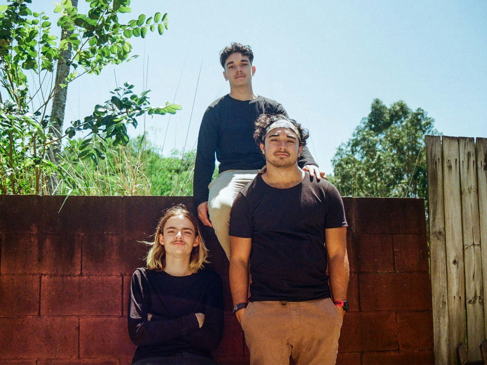 Members of Tjaka stand against a red brick wall, with one sitting on top.