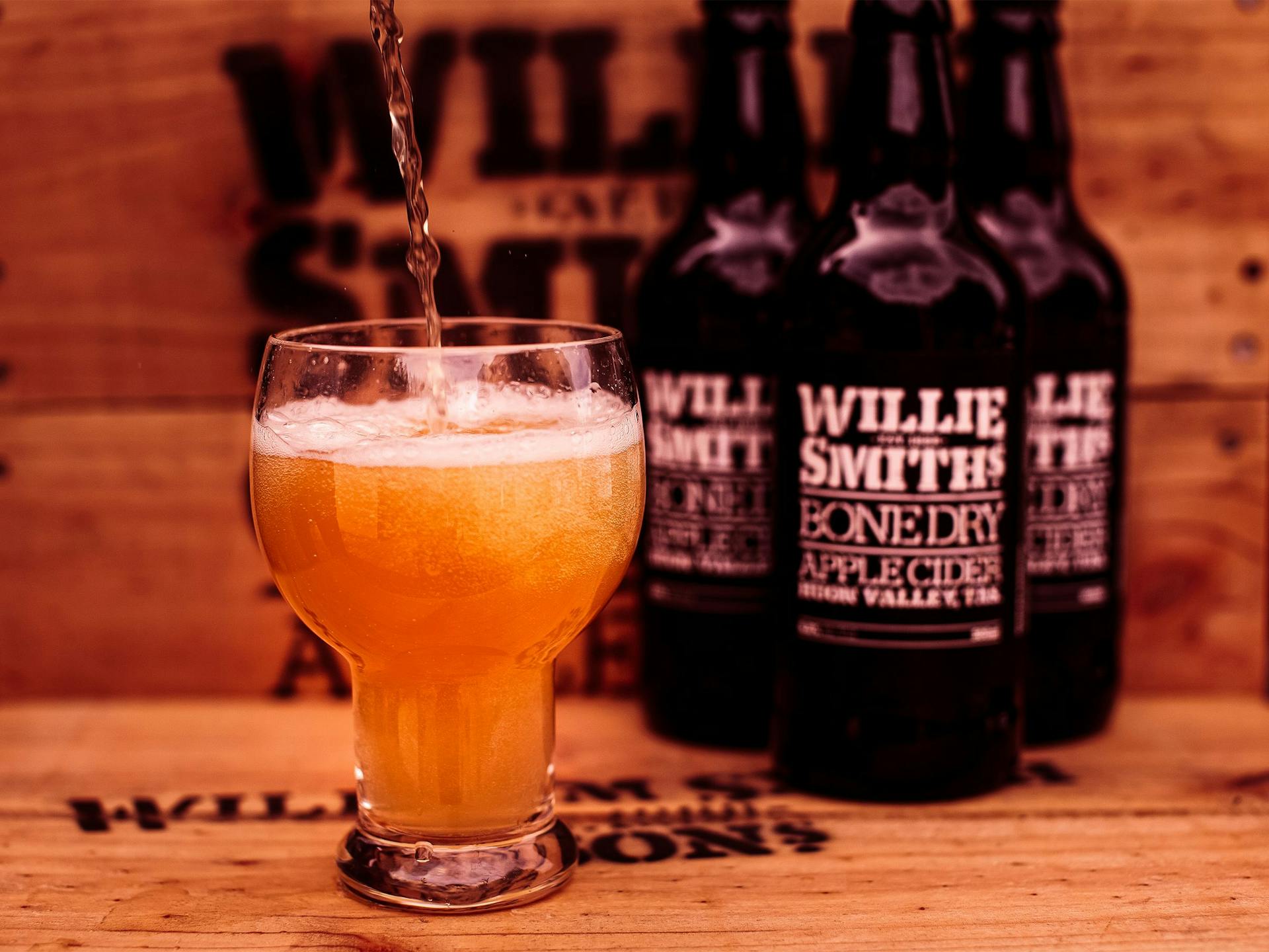 Three bottles and a glass of cider sitting on an apple crate