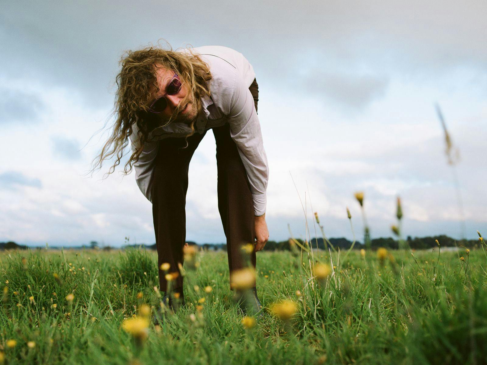 Our Carlson leans over forward, reaching down to a field of grass and yellow flowers.