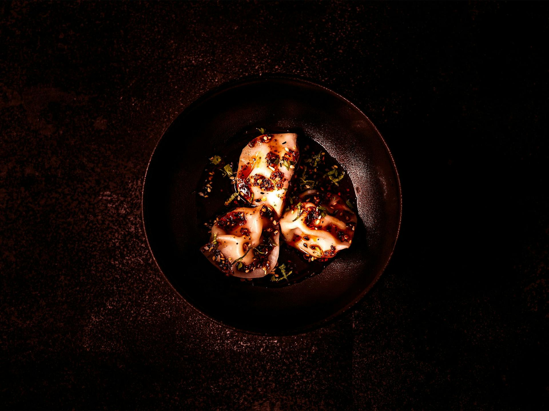 A bowl of three sea urchin dumplings sitting in dipping sauce, sprinkled with spring onion