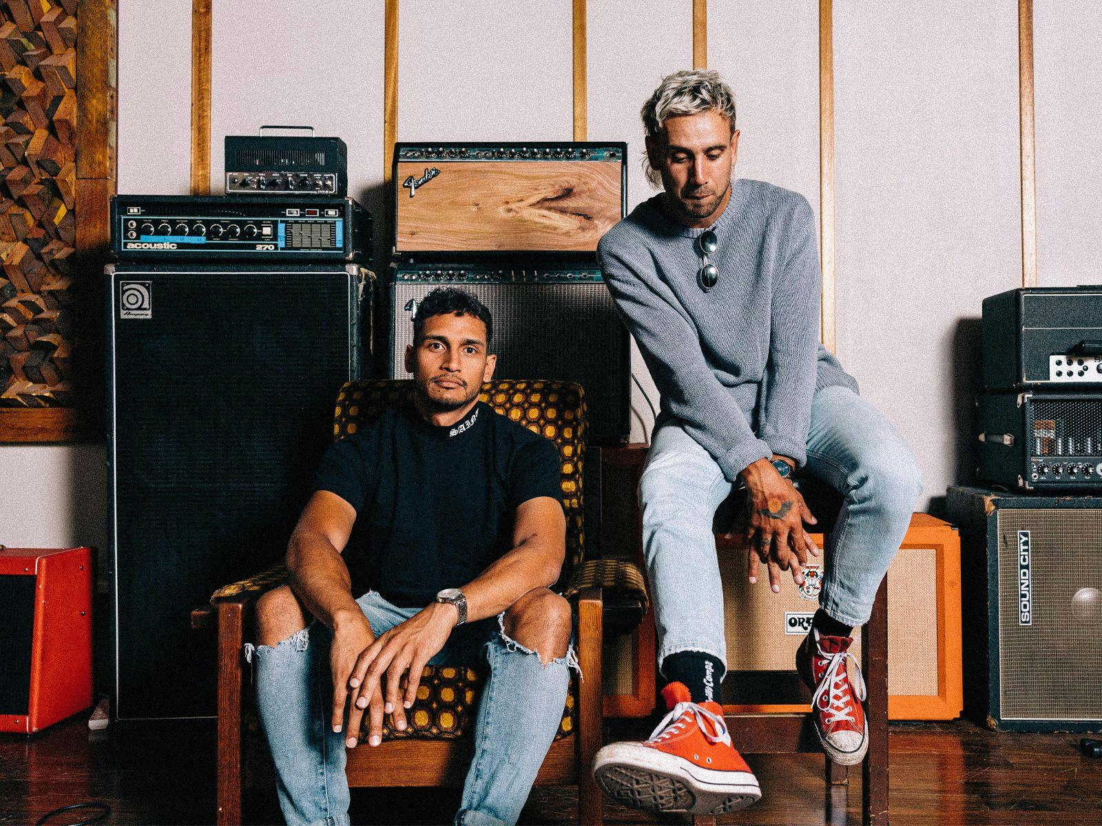 MARLON X RULLA seated on chairs, several large amps behind them.