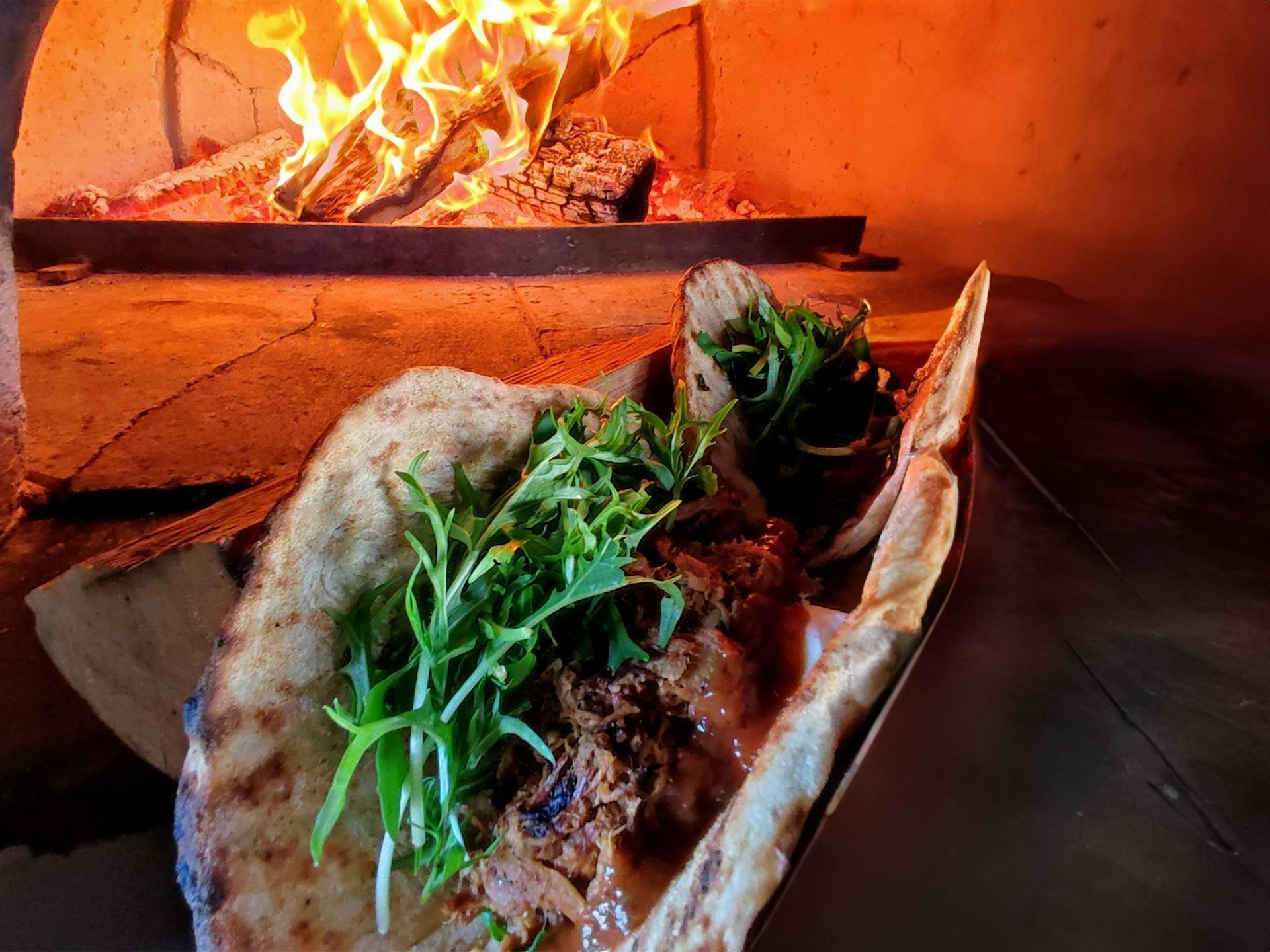 A woodfired flatbread with a topping of meat, onion, sour cream and parsley