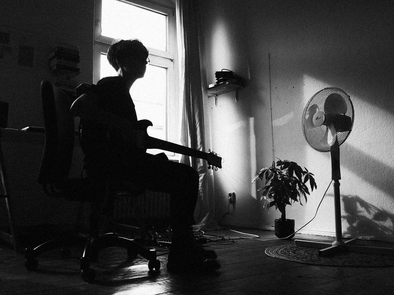 Julia Reidy sits on an office chair with a guitar on their lap.