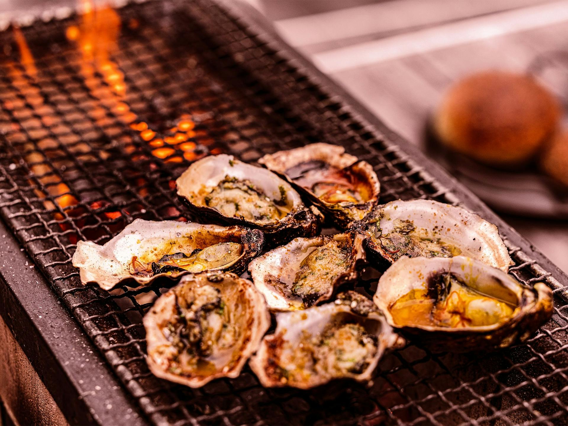 A bunch of woodfired oysters grilling on a hibachi with flames in the background