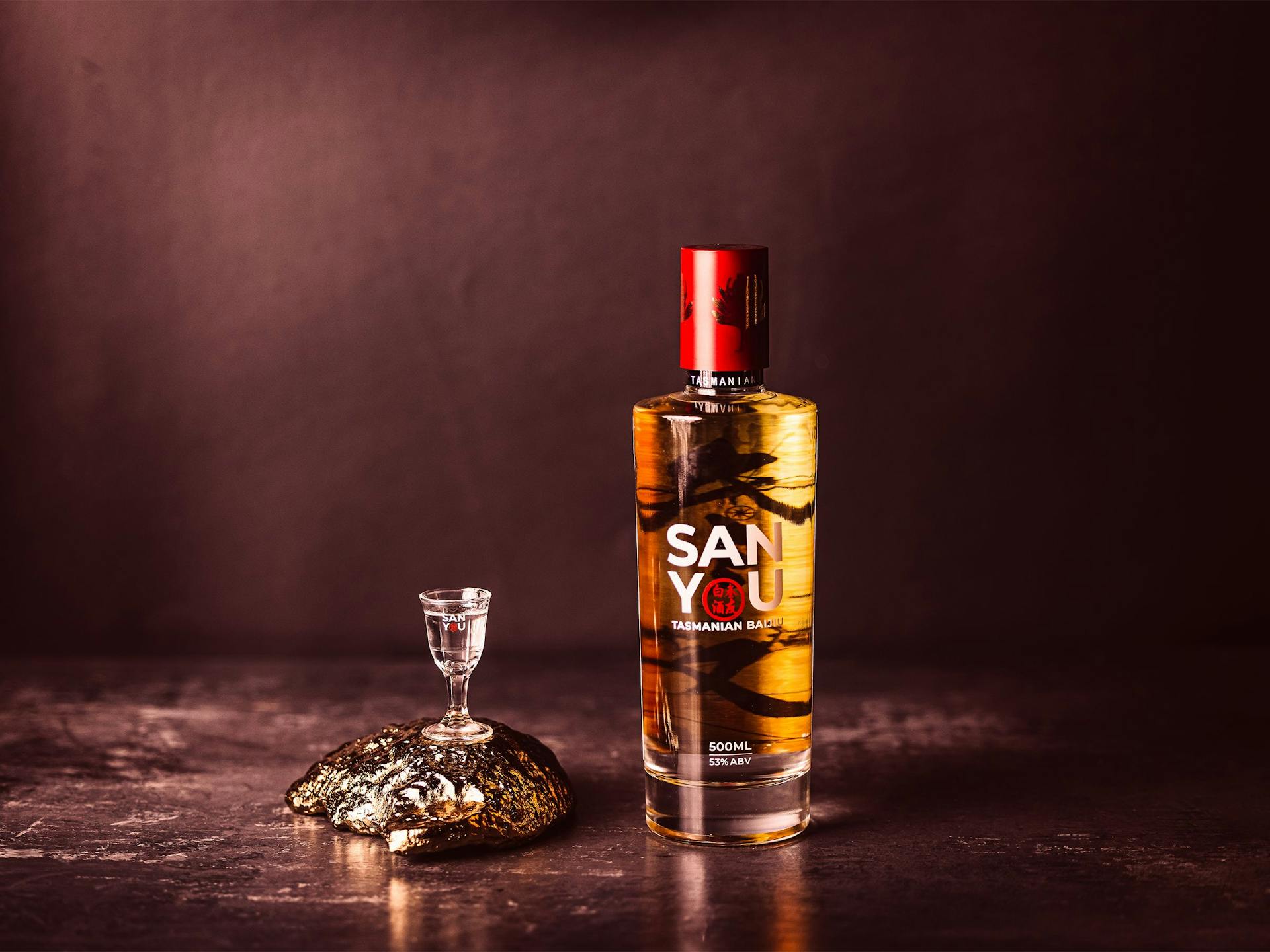 A bottle of baijiu sitting next to a small baijiu glass that rests upon a golden oyster shell