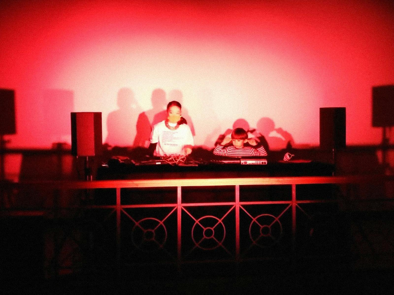 Tujiko Noriko performing on DJ decks, bathed in red lights.