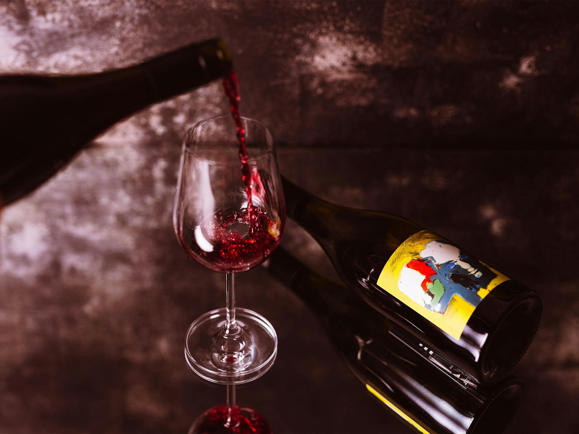 A glass of red wine being poured on a mirrored surface. 