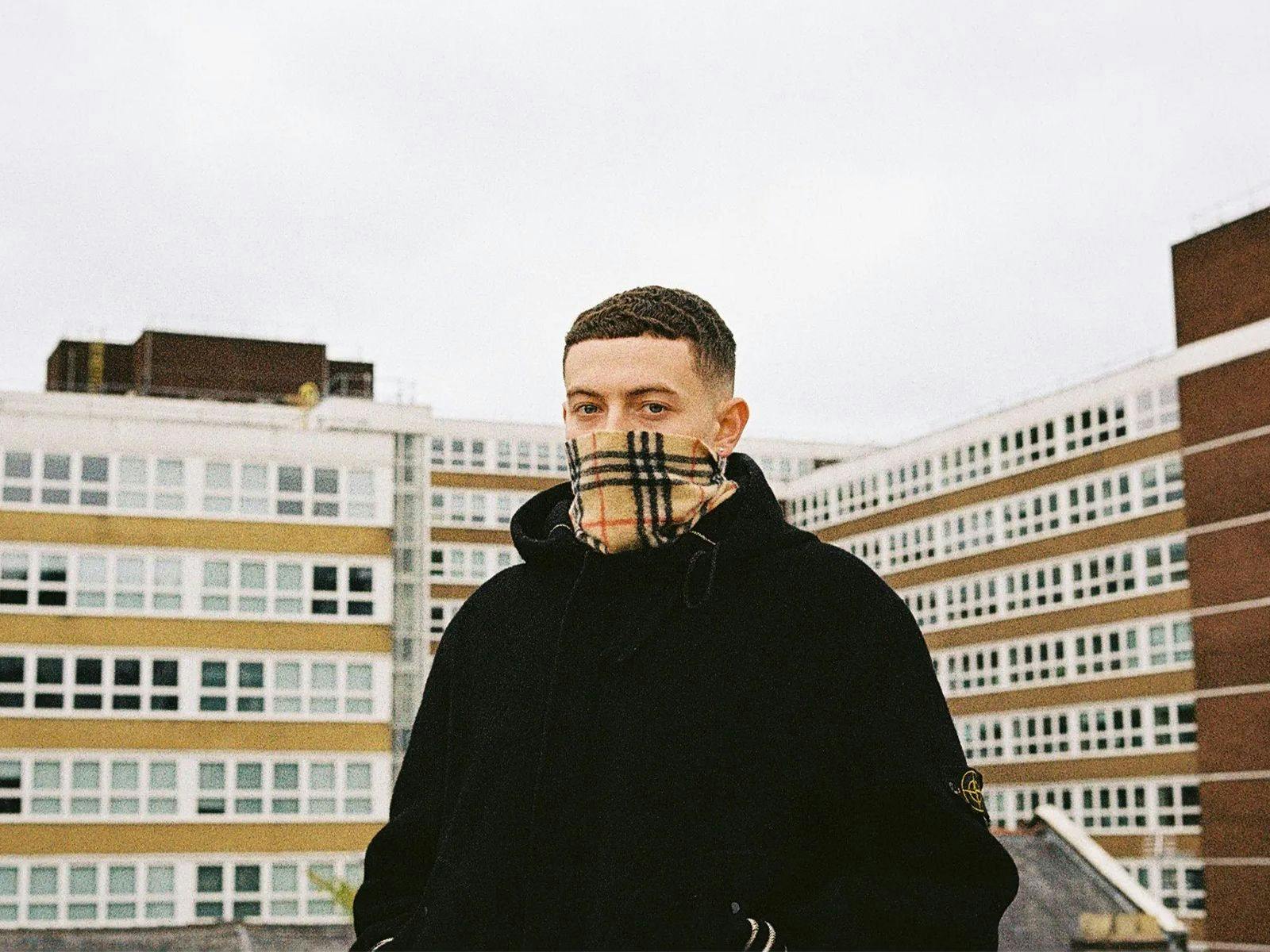 Rainy Miller wearing a tartan scarf and black jumper, behind them large buildings.