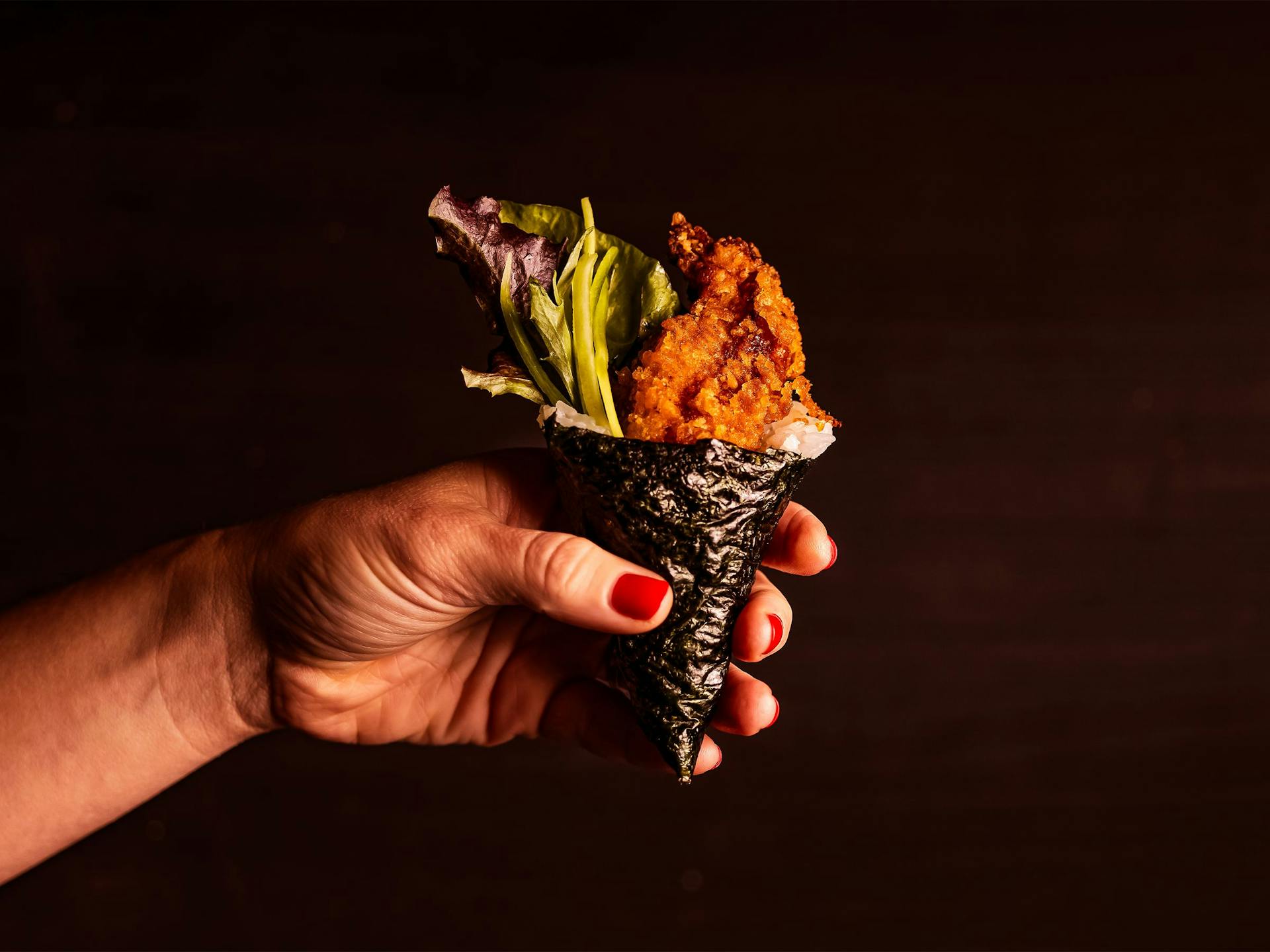 A hand holding up a hand roll sushi