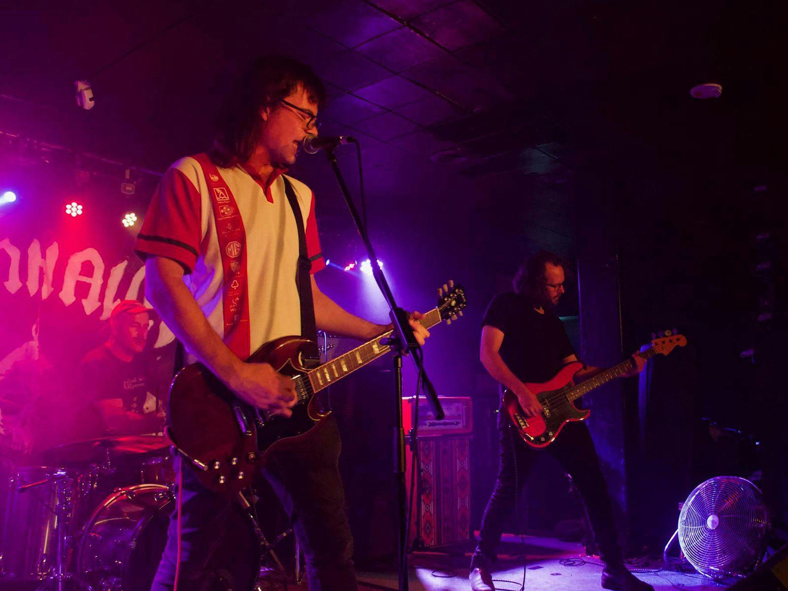 Liquid Nails guitarists performing on-stage bathed in red and purple light.