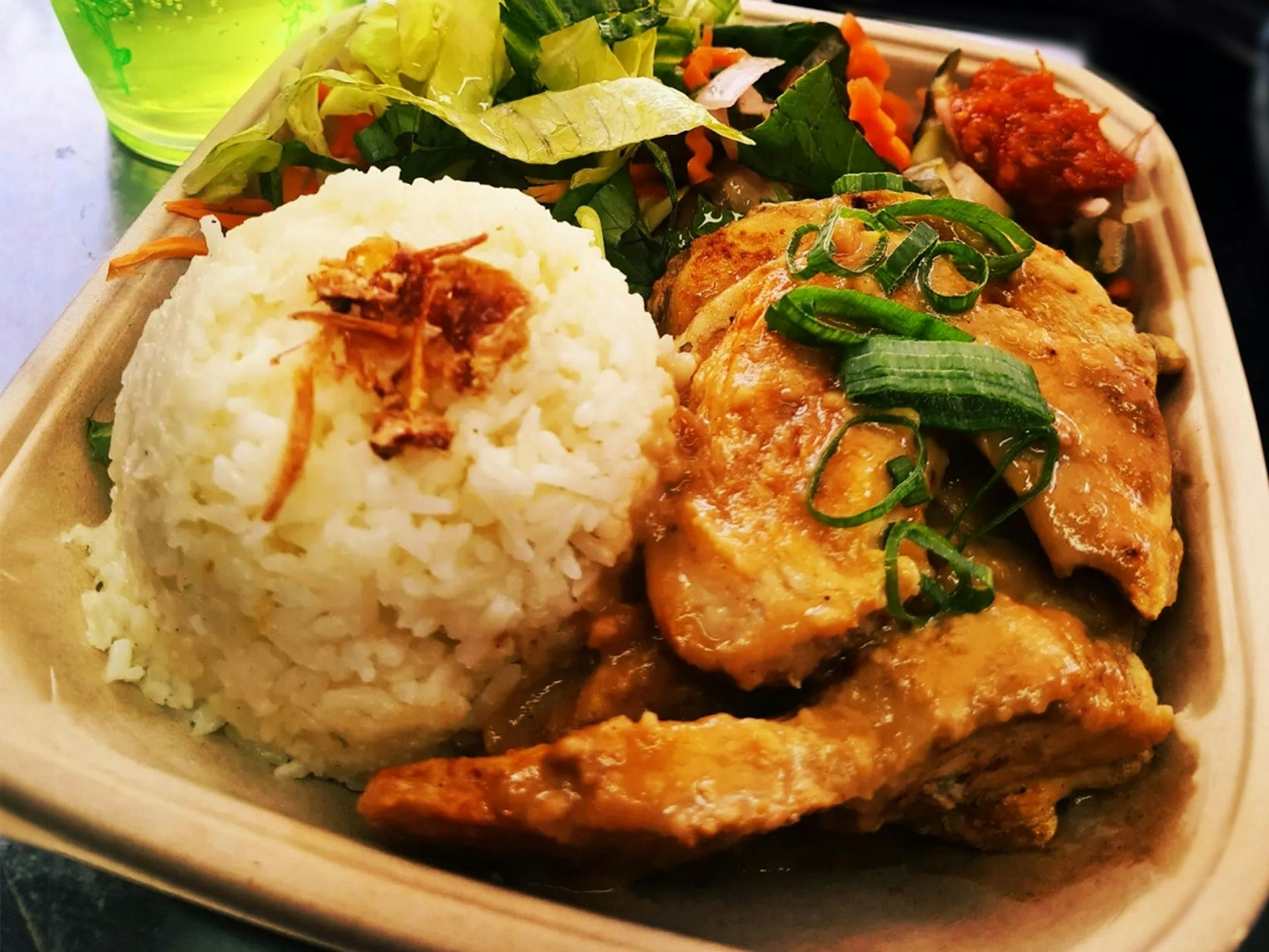 Grilled chicken and rice in a takeaway container with salad