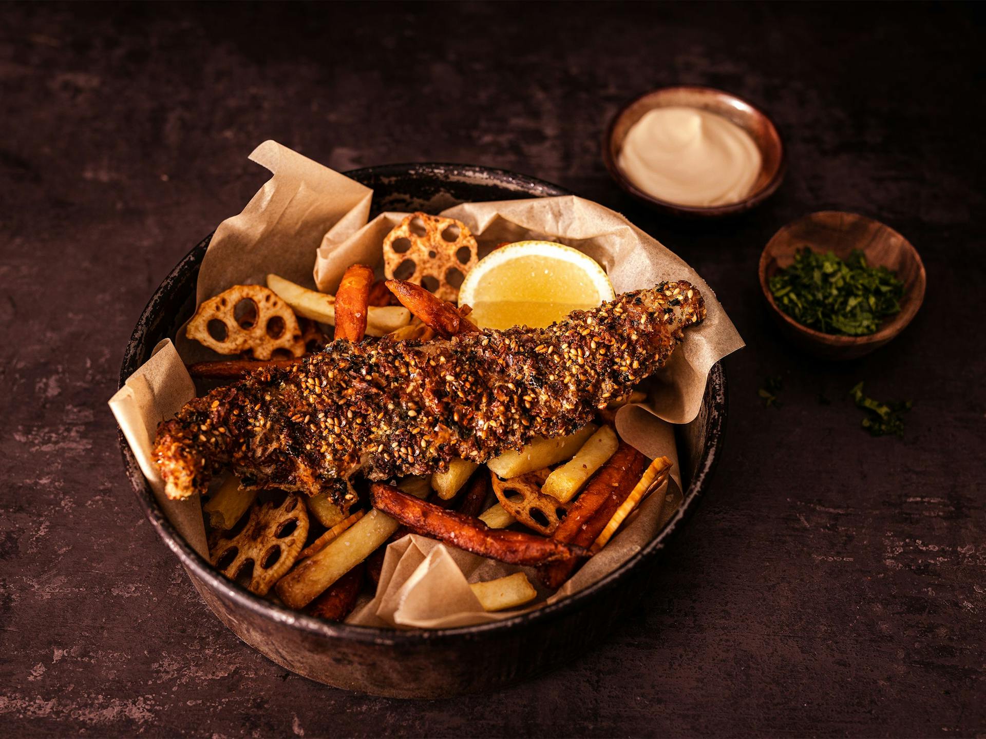 Sesame-crumbed fish lies on a bed of mixed chips of sweet potato, lotus and potato