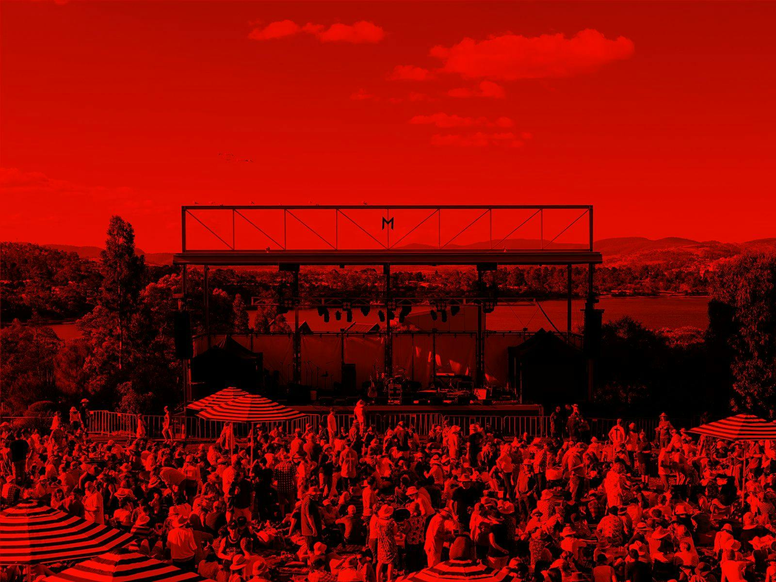 A red-washed image of hundreds of people relaxing, drinking and listening to music on the lawns at Mona.