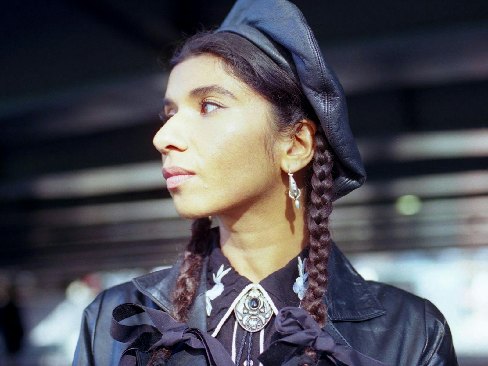 Nabihah Iqbal looks to their side, wearing a leather jacket and cap.