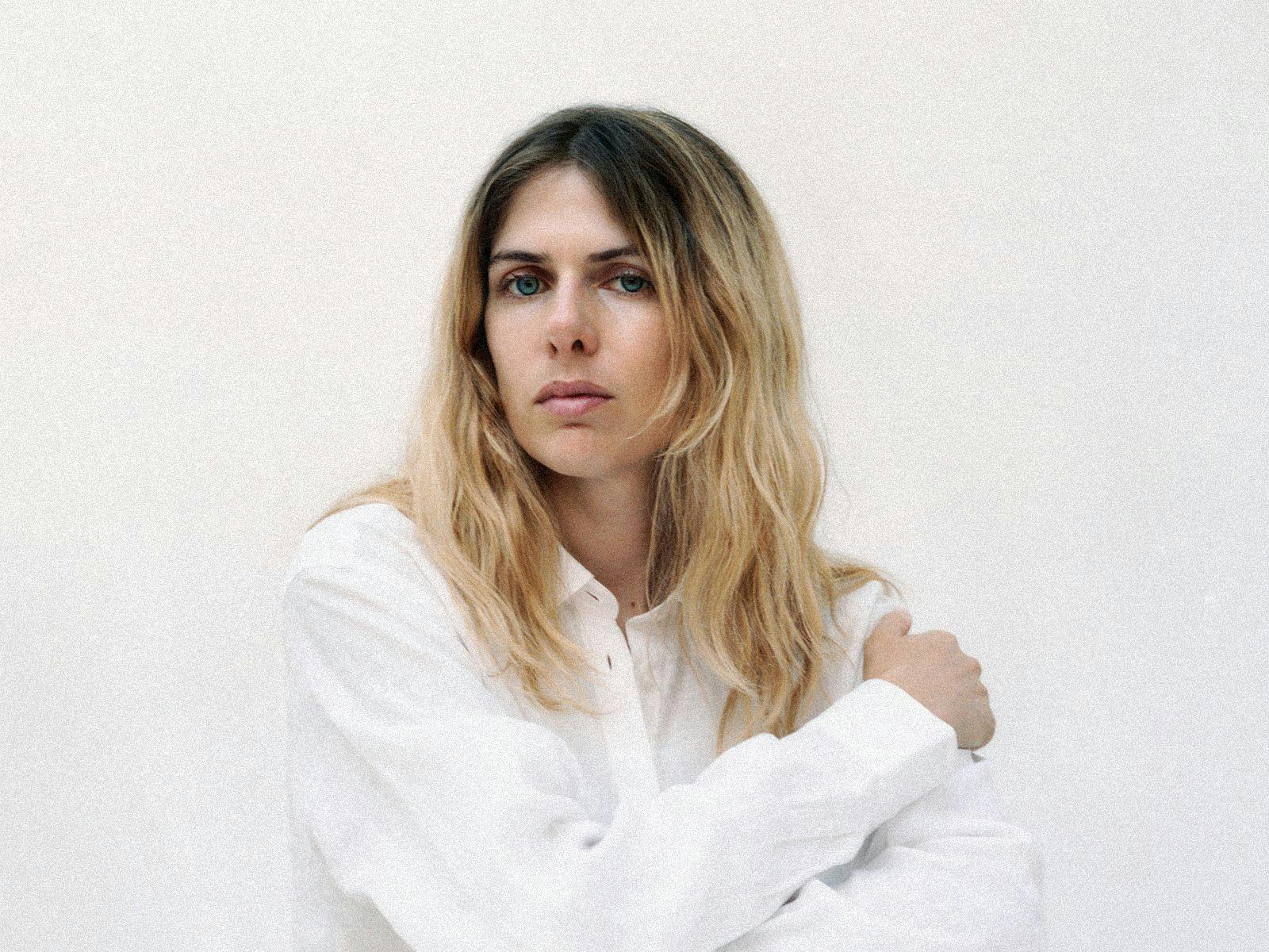 Laurel Halo poses in a white long sleeve shirt with arms crossed.