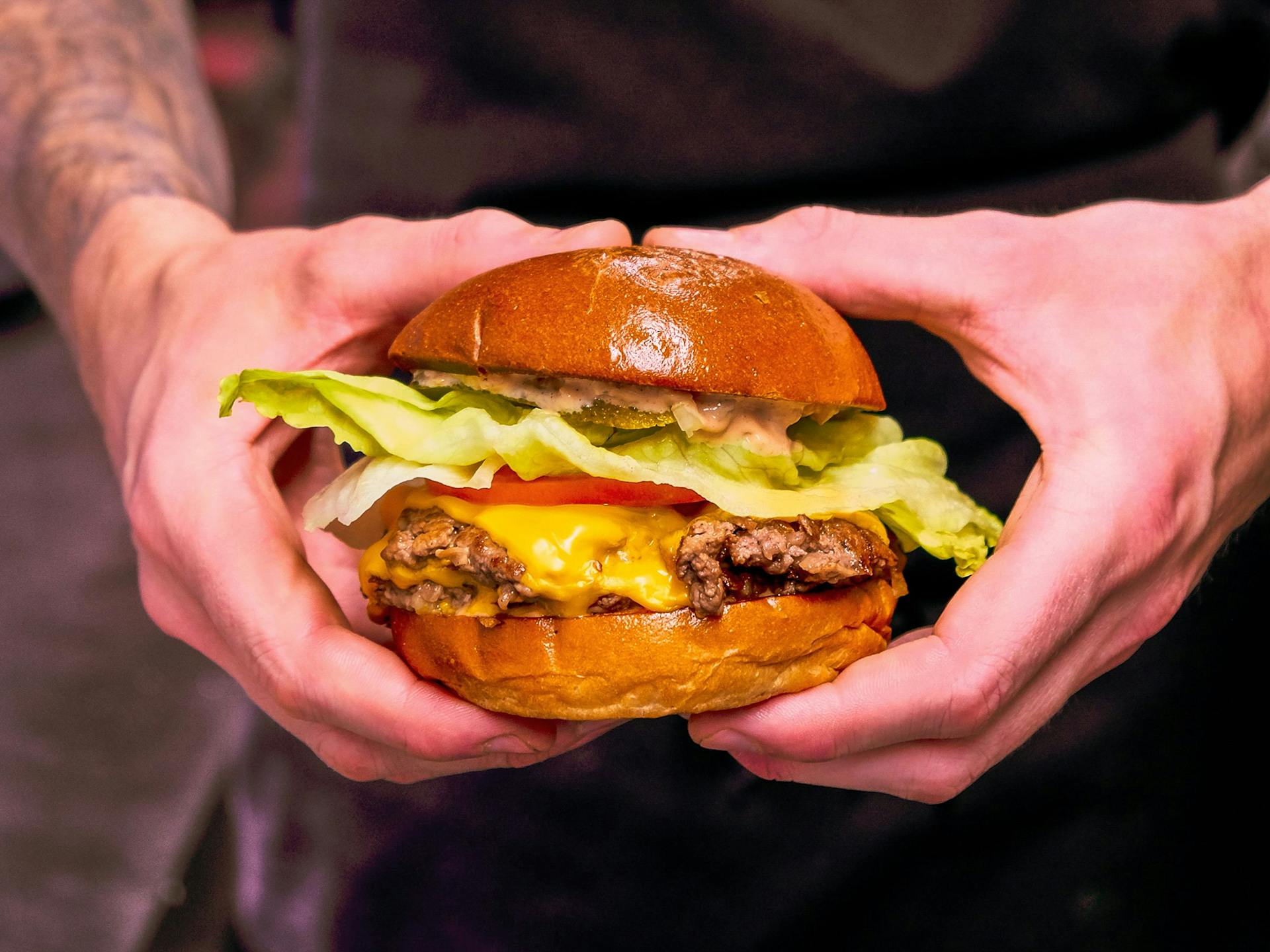 A man with arm tattoos holding a cheeseburger