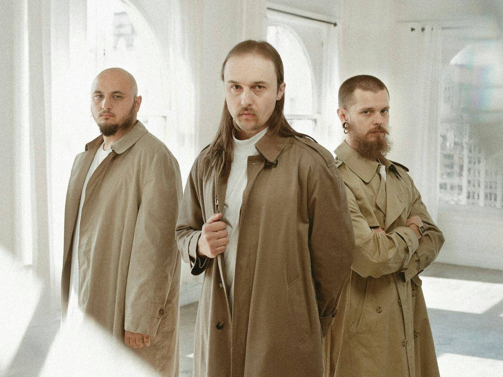 Members of Molchat Doma posing, wearing long brown trenchcoats.