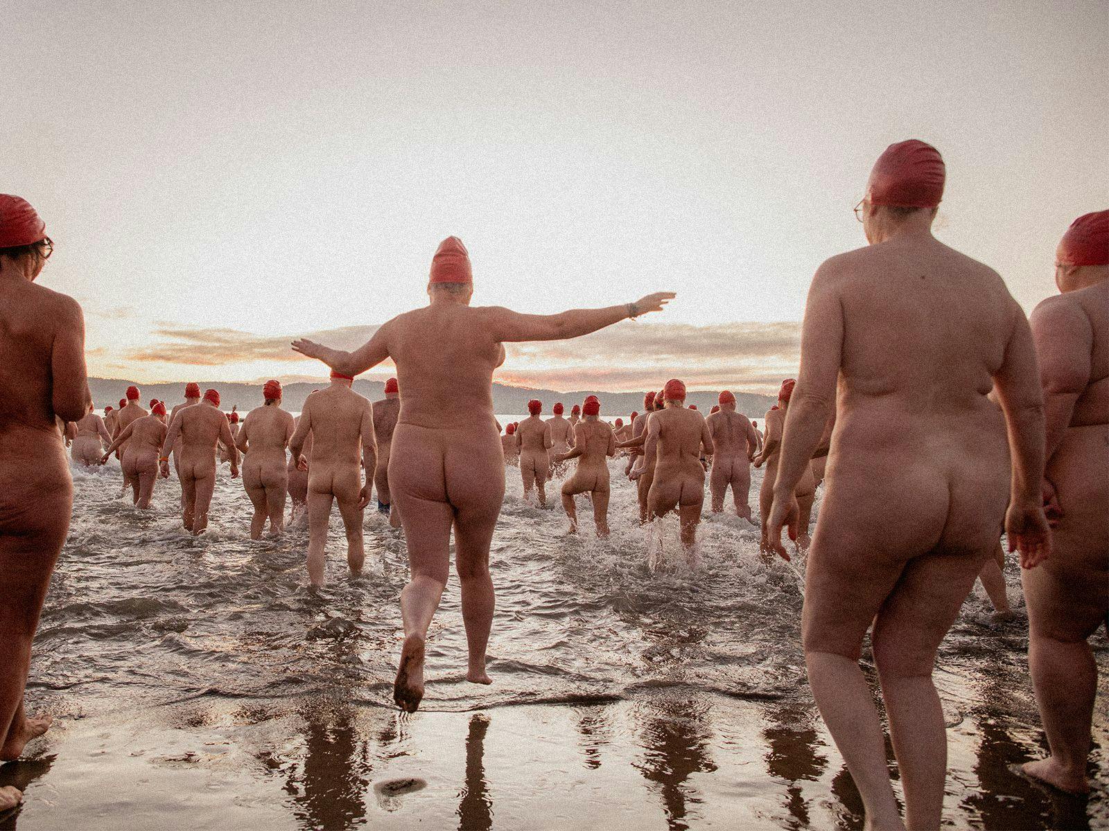 Several nude people running into the ocean at sunrise.