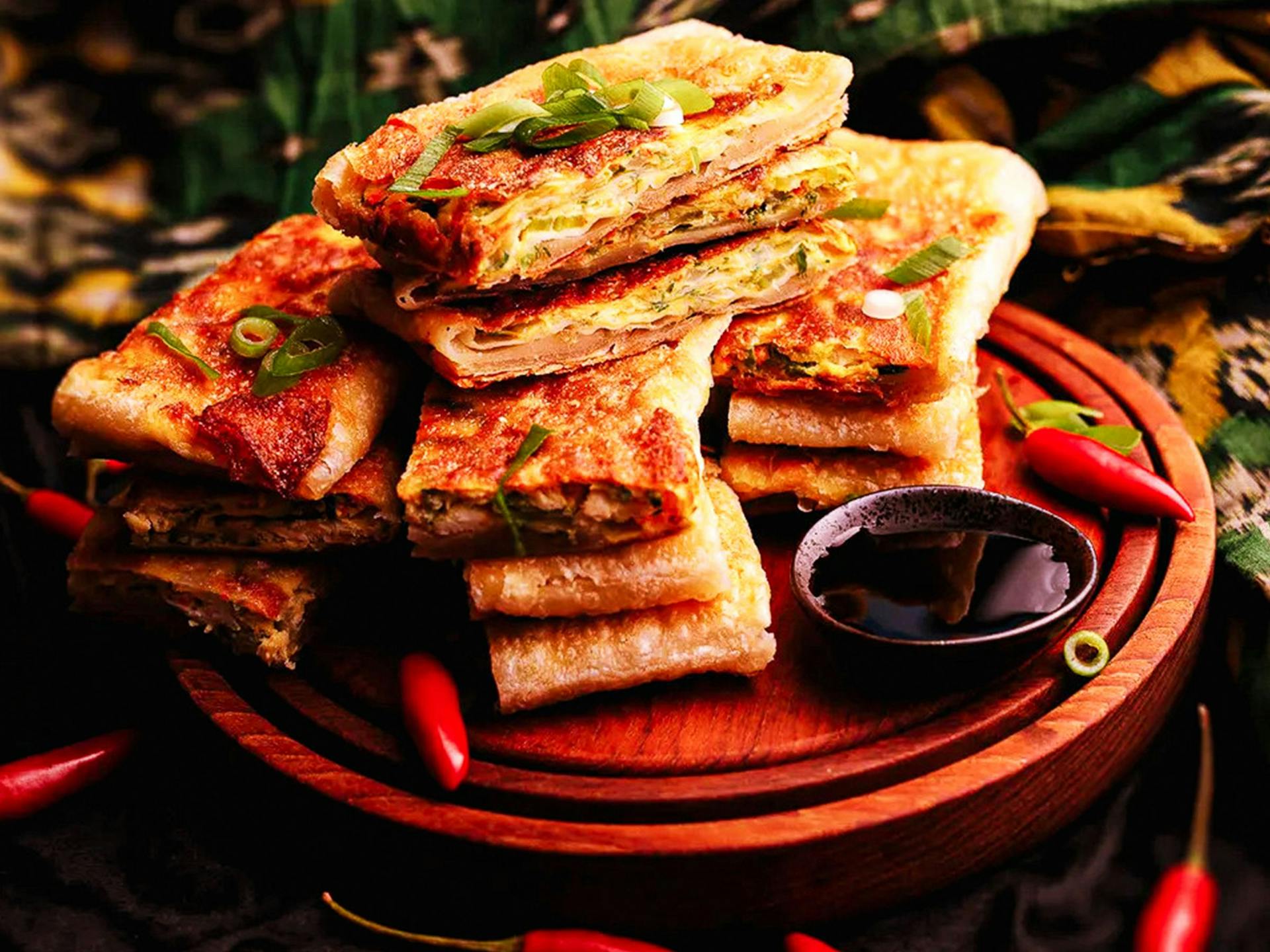 A big pile of Indonesian Martabak on a wooden board with a dipping sauce