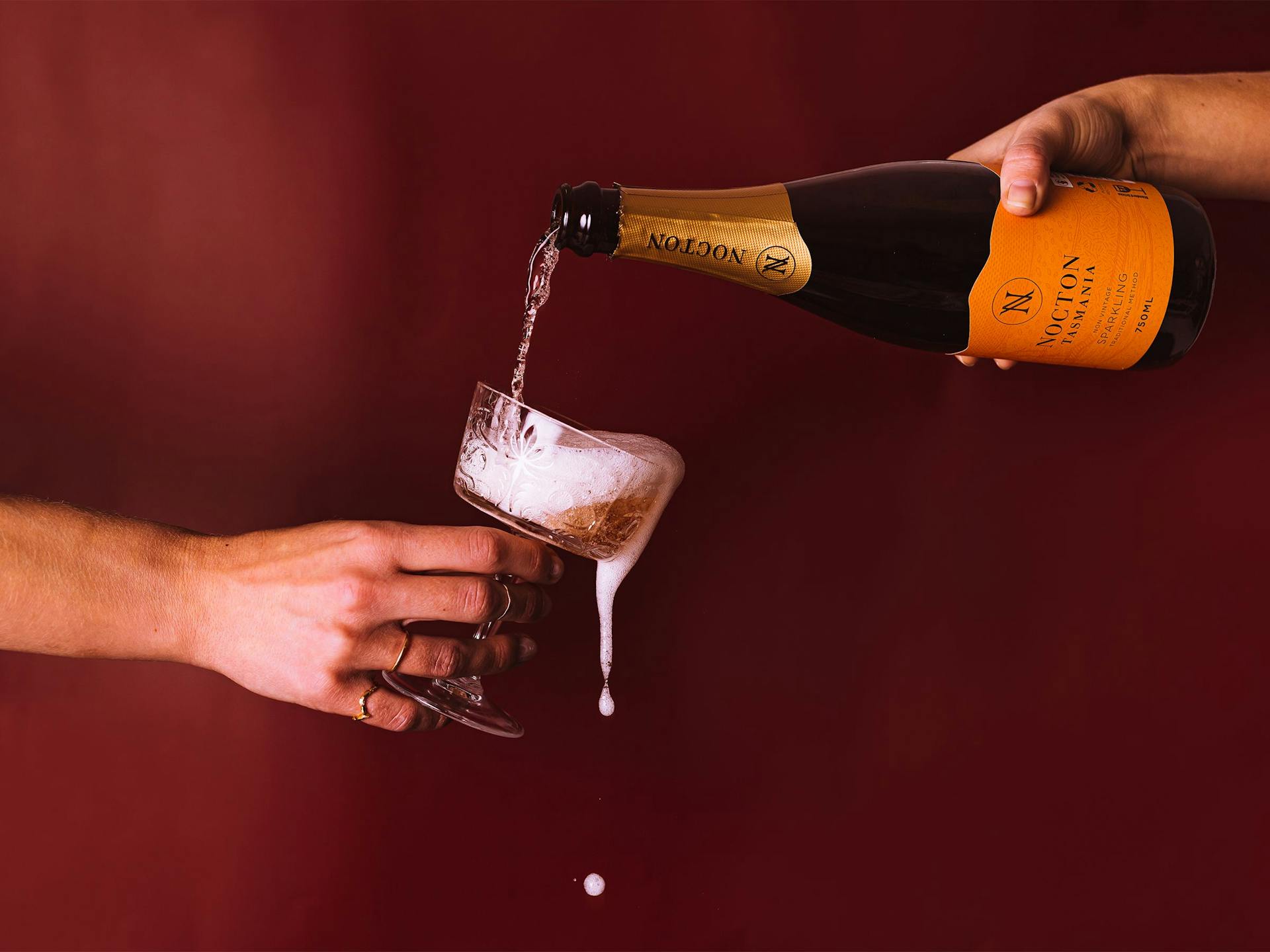 A bottle of sparkling wine pouring into an overflowing coupe glass