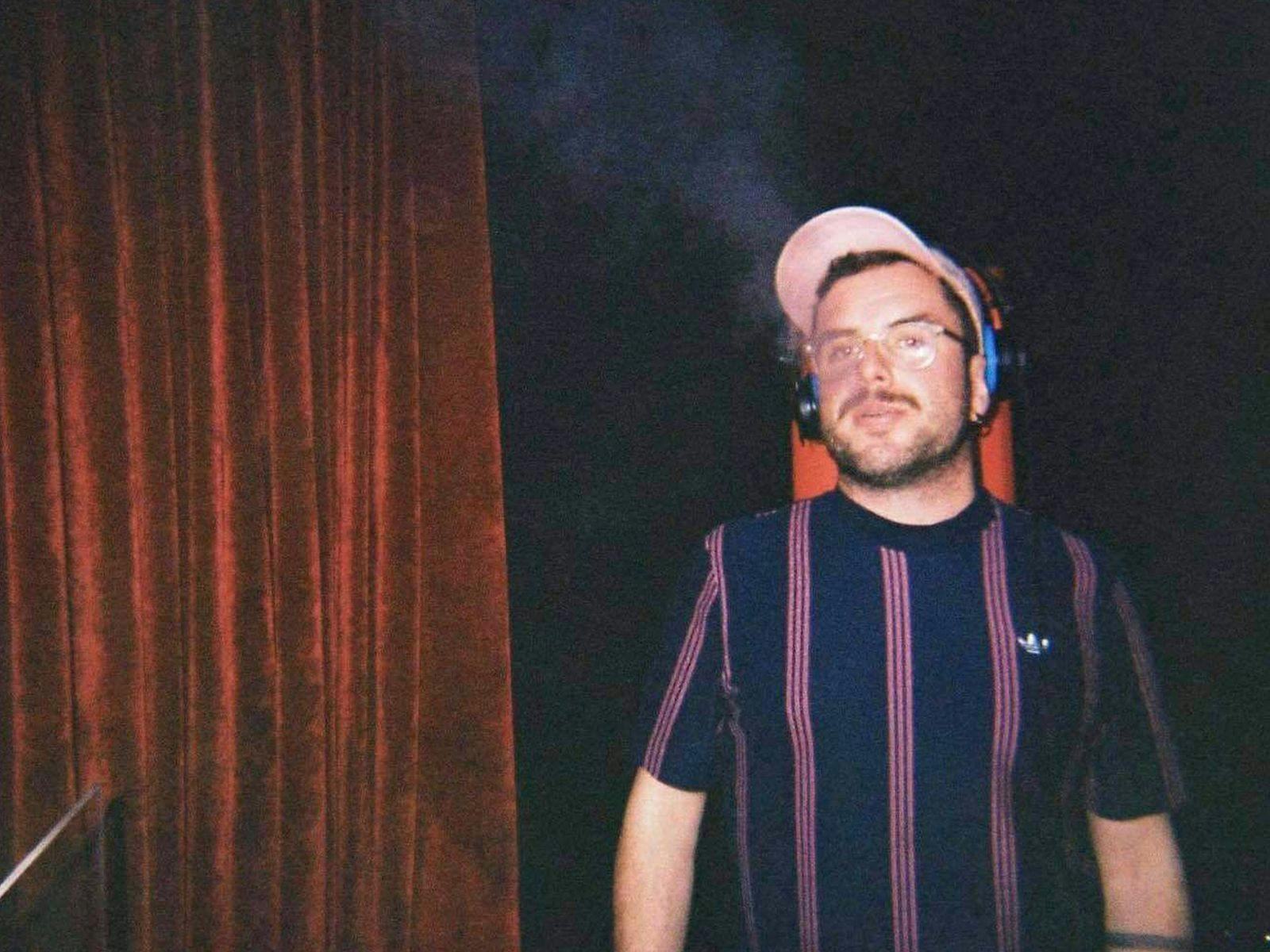 Alex Morris in a dimly lit room, wearing a hat and headphones.