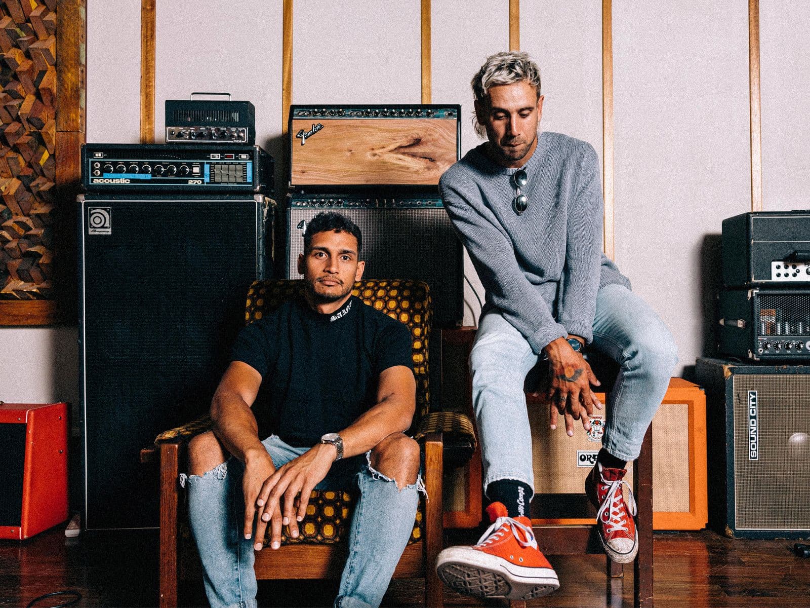 MARLON X RULLA seated on chairs, several large amps behind them.