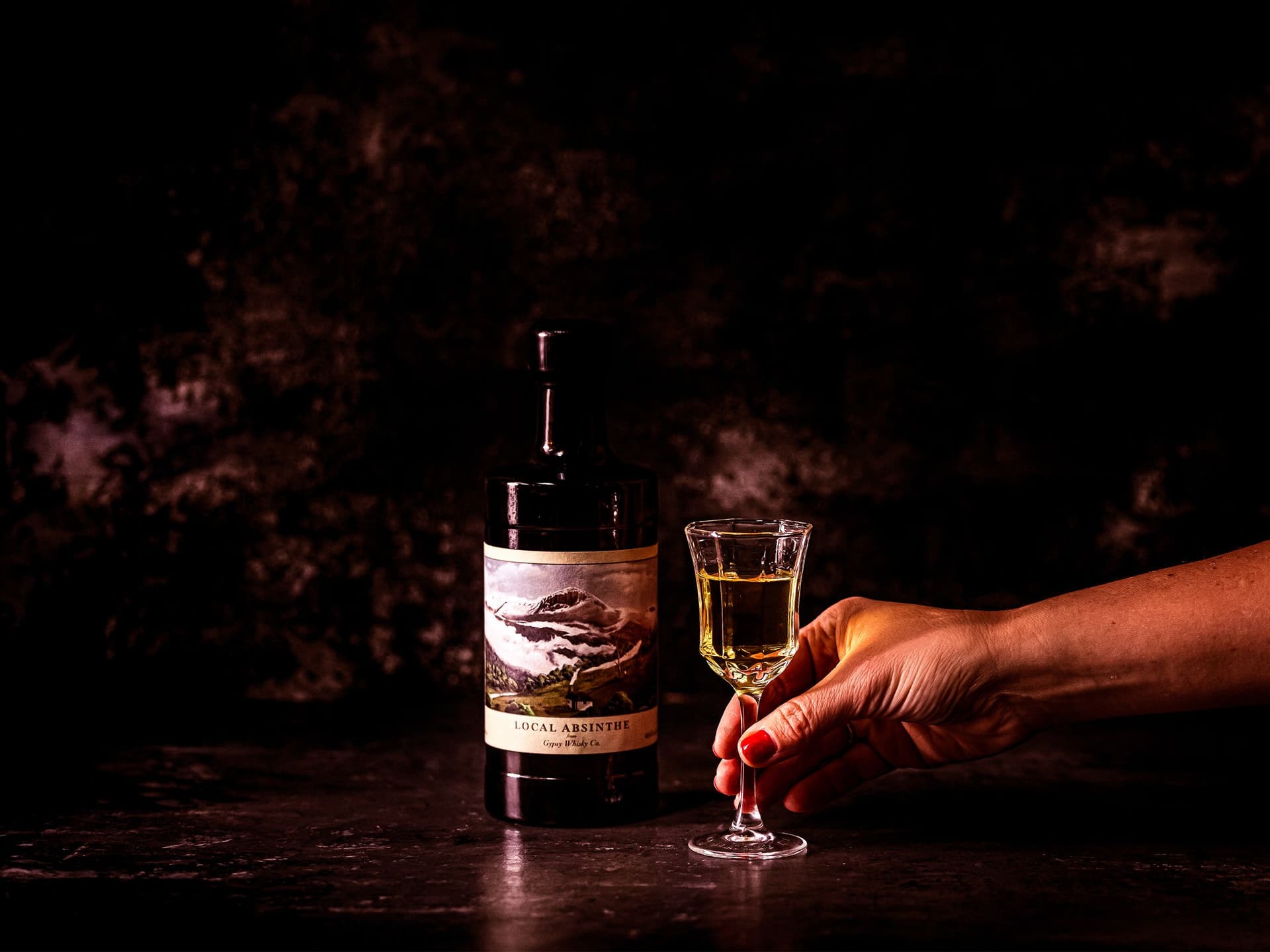 A bottle and glass of absinthe with a hand reaching in