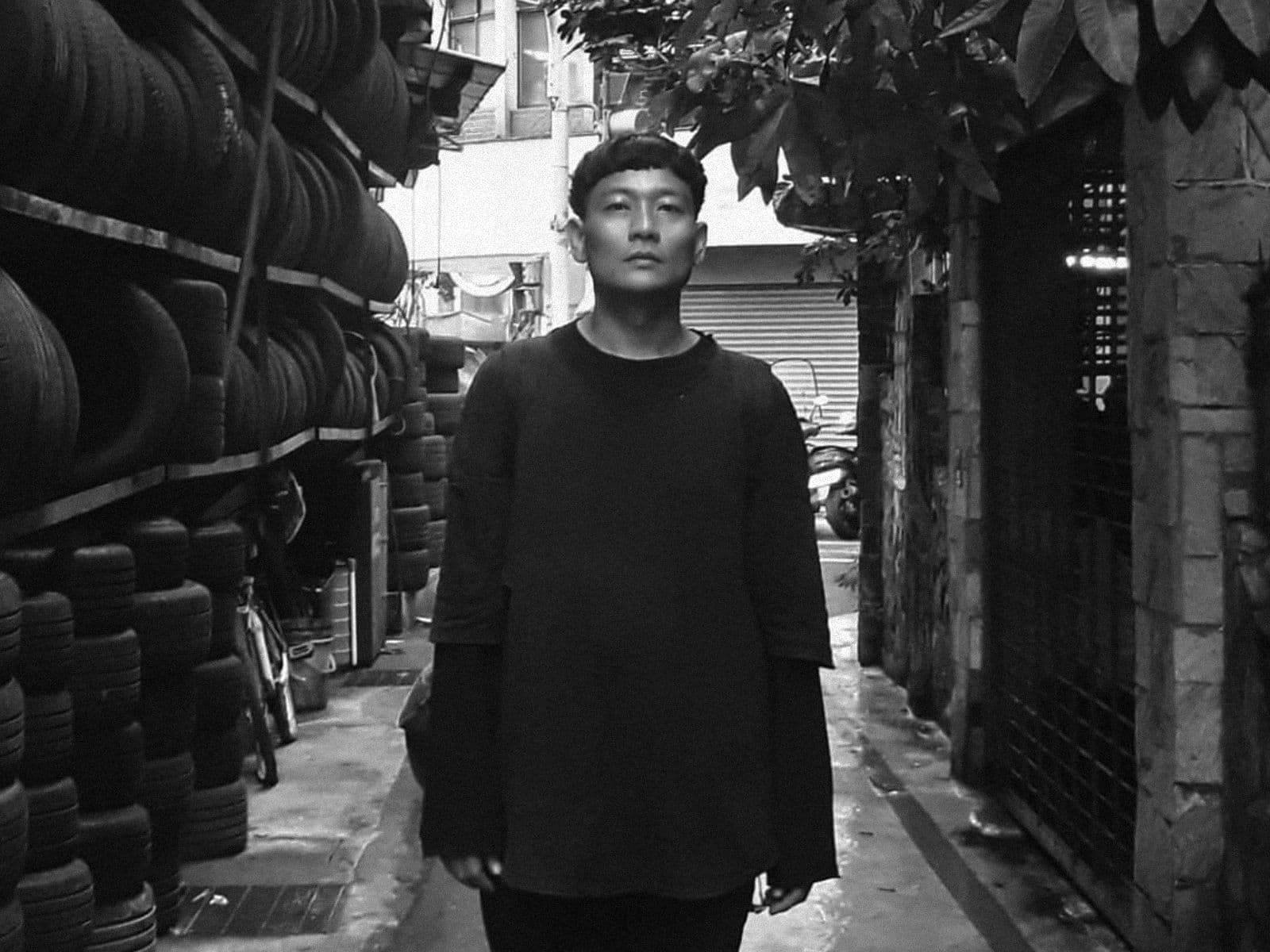 Kasimyn standing in the street, hundreds of tyres are stacked up to their left.