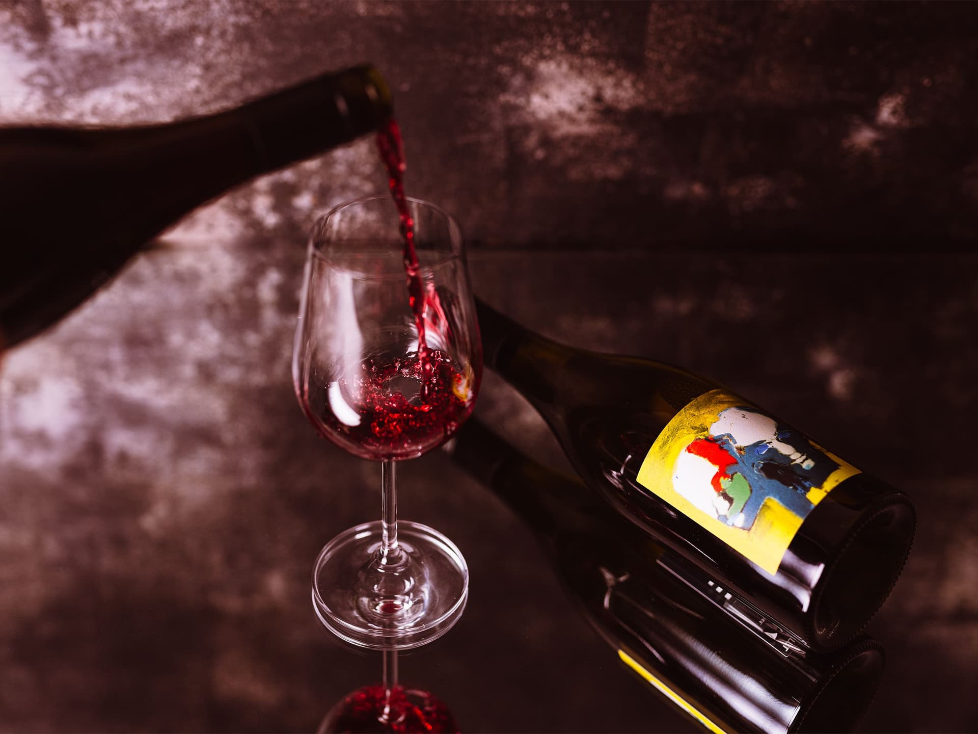 A glass of red wine being poured on a mirrored surface.