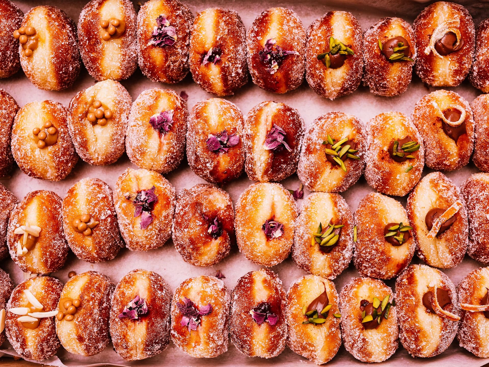 Dozens of donuts lie face up with jam and other fillings on display