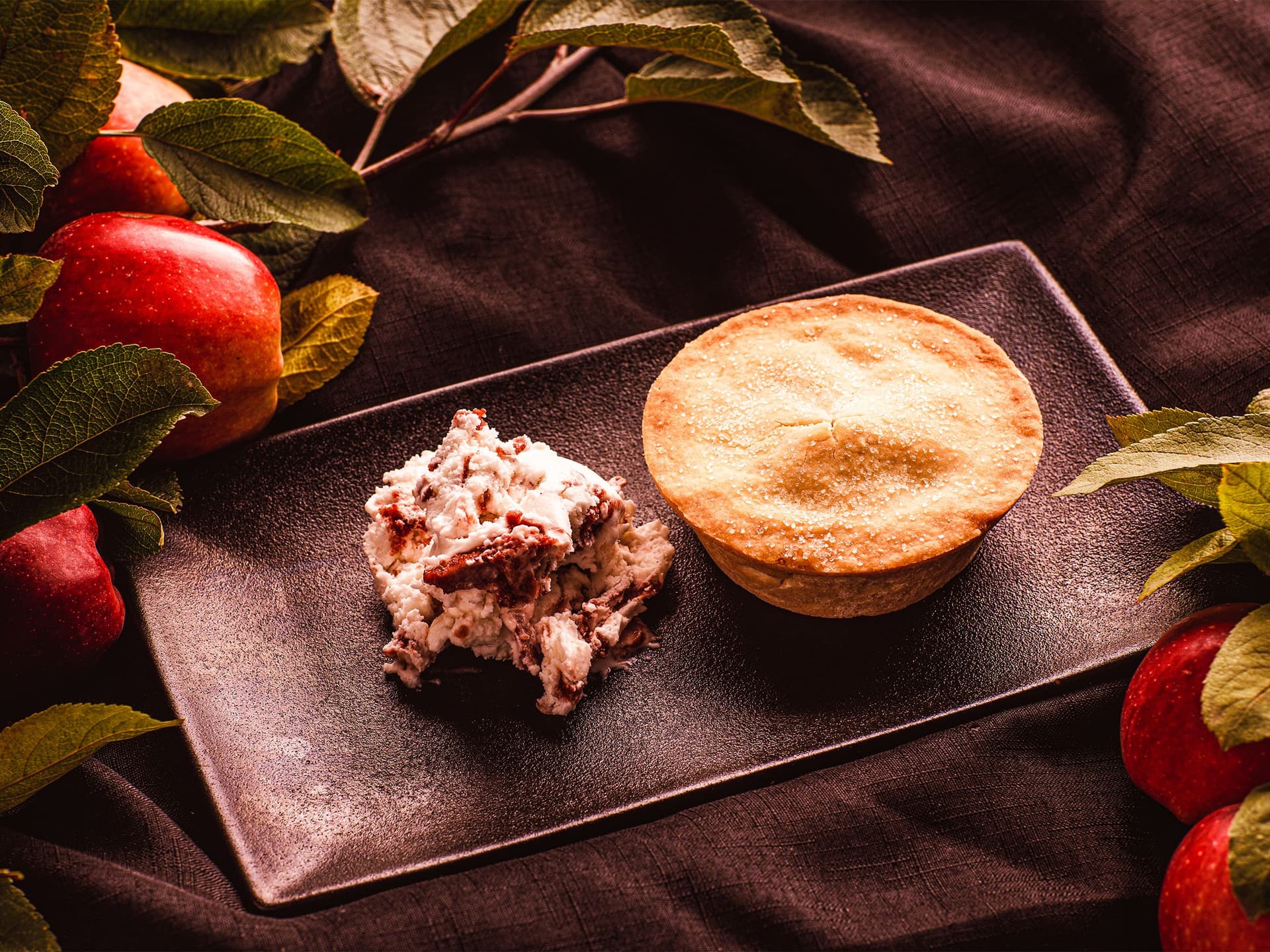 Fresh apples surround a plate with a hot apple pie and vanilla ice cream