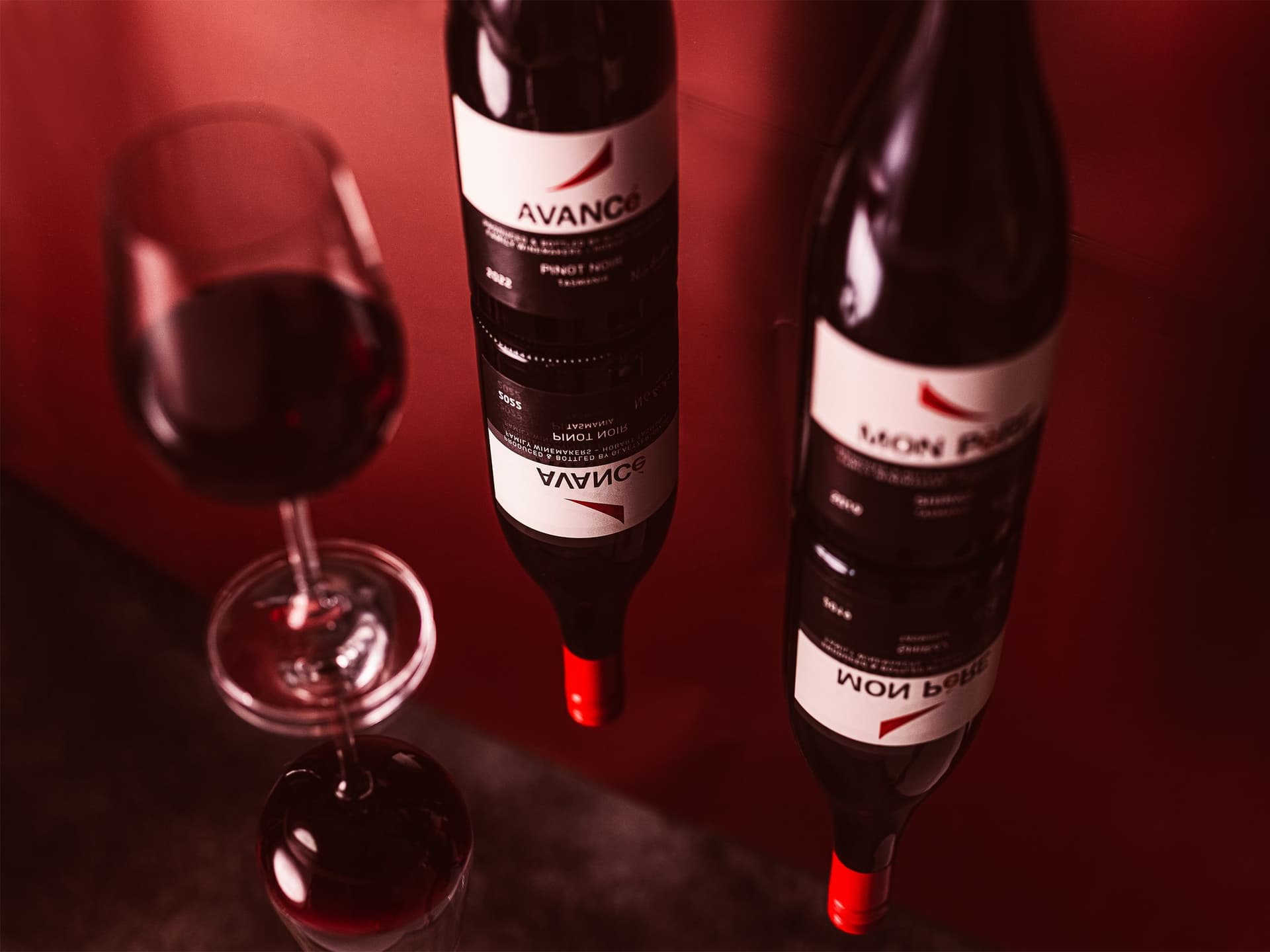 Two wine bottles and a glass of red wine reflected in a mirror