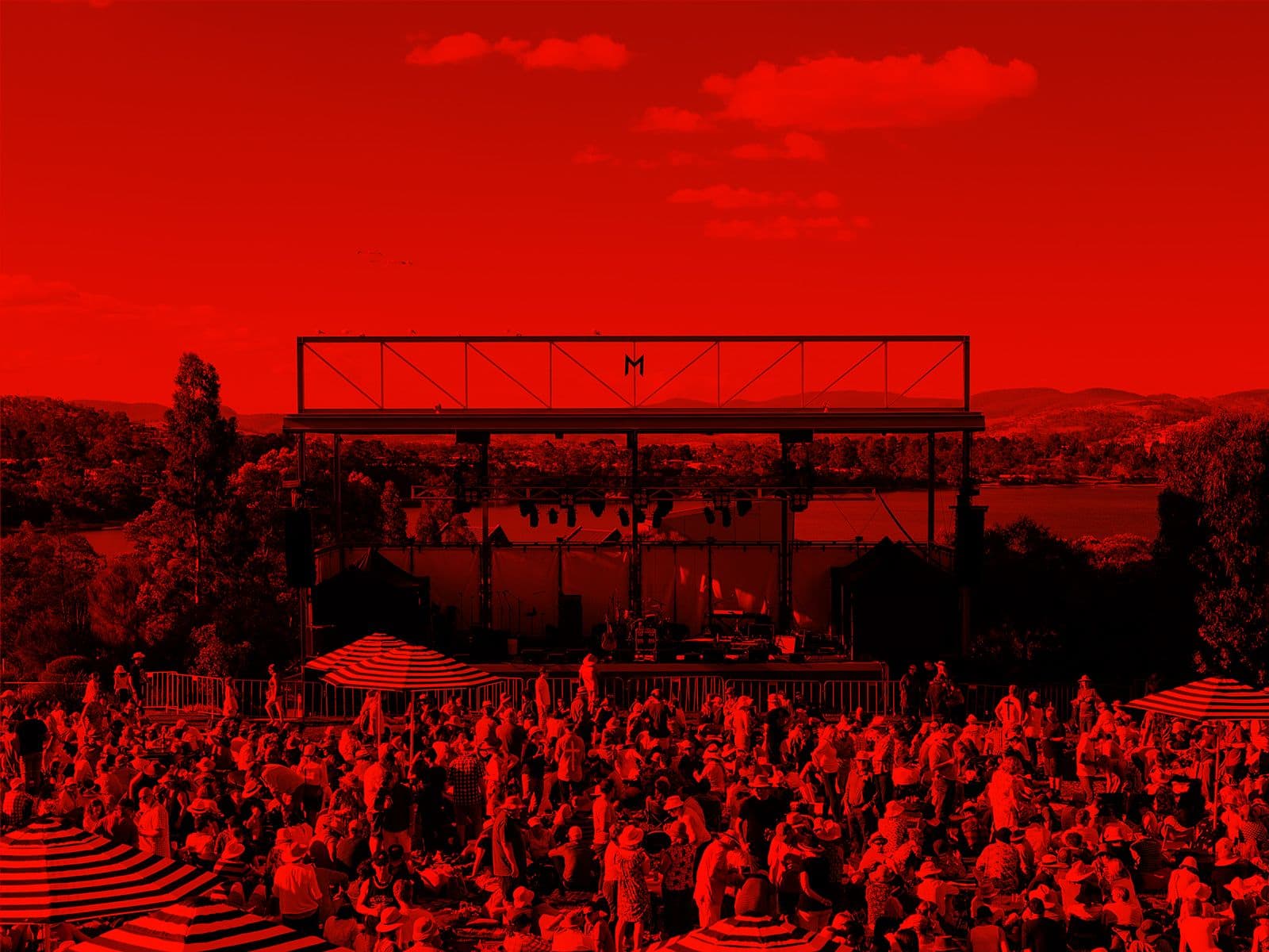 A red-washed image of hundreds of people relaxing, drinking and listening to music on the lawns at Mona.
