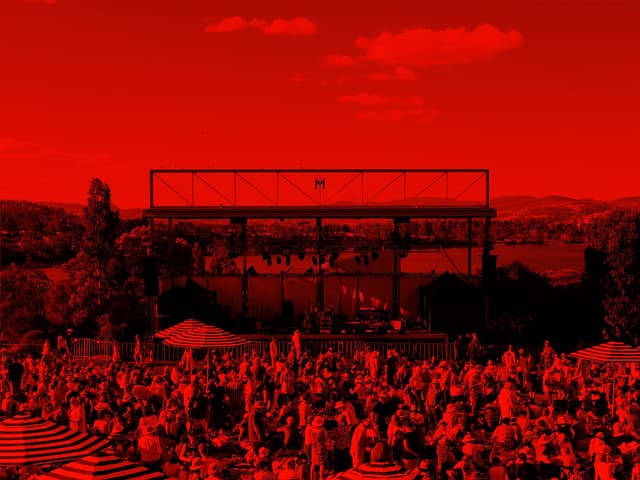 A red-washed image of hundreds of people relaxing, drinking and listening to music on the lawns at Mona.