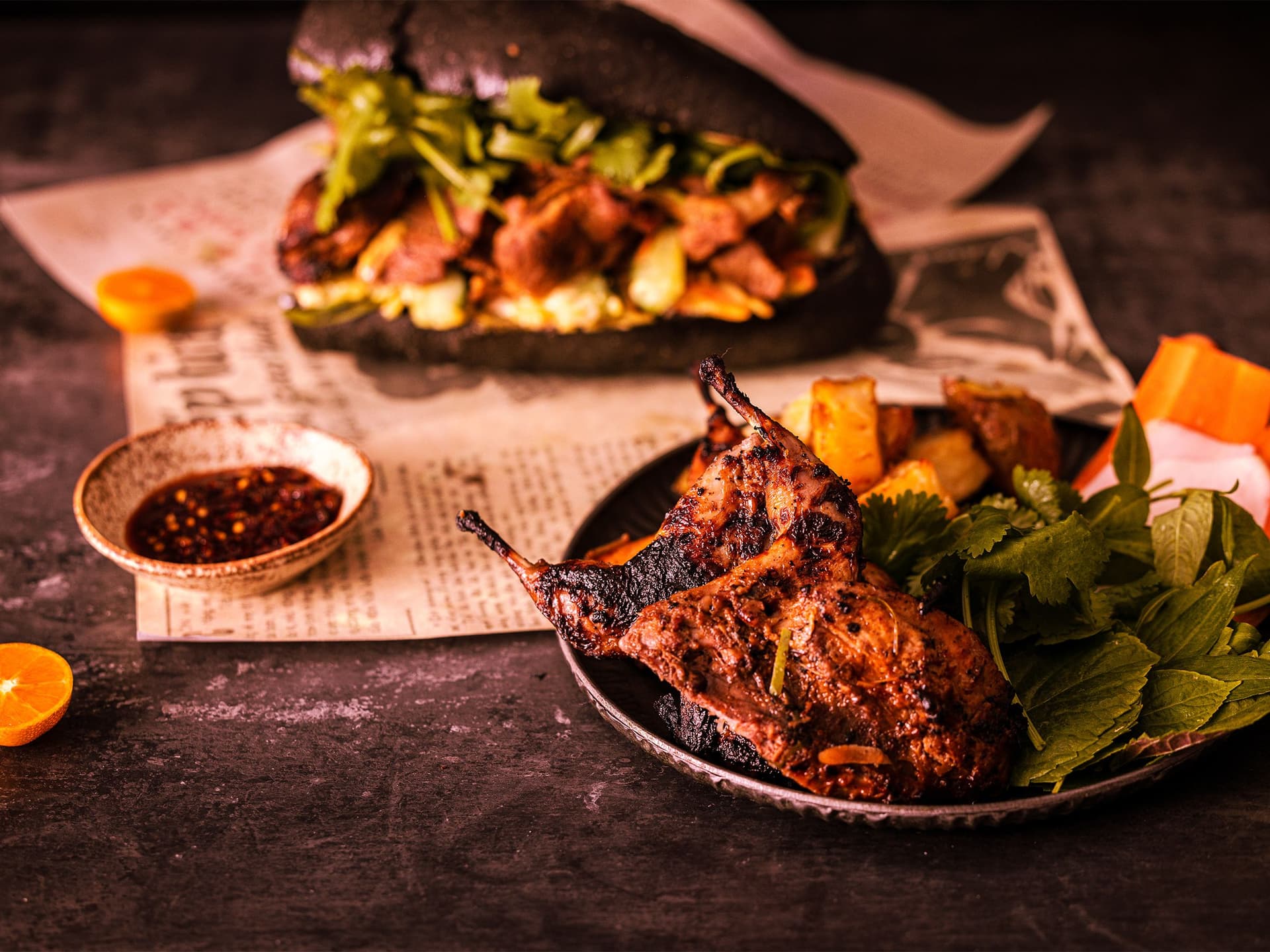 Chargrilled quail and salad on a plate in front of an out of focus banh mi