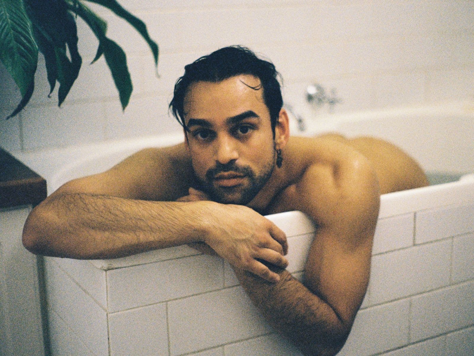 Aqueerius lies in their bathtub, arms hung over the edge.